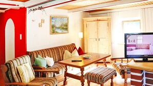 A cozy living room with a sofa, a wooden dining table, a television, and a cabinet. - Farmhouse in Kossen Near Kitzbuhel Alps (Koessen)
