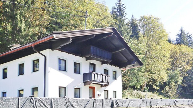 A white building with a sloped roof, a balcony, and a stone wall in front. - Farmhouse in Kossen Near Kitzbuhel Alps (Koessen)