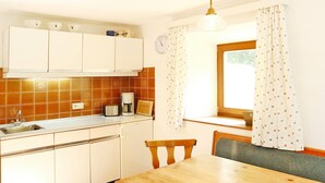 A kitchen with white cabinets, a wooden table, and a window with curtains. - Farmhouse in Kossen Near Kitzbuhel Alps (Koessen)