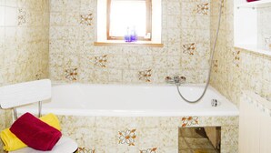 A bathroom with a bathtub, a shower, and a window with a bottle on the windowsill. - Farmhouse in Kossen Near Kitzbuhel Alps (Koessen)
