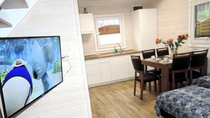 Ein gemütlicher Raum mit Bett, Esstisch mit Stühlen, Küchenzeile und einem an der Wand befestigten Fernseher.