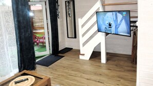 Ein Wohnzimmer mit Holzboden, einem an der Wand befestigten Fernseher, einer Treppe und einer zur Außenseite führenden Tür.