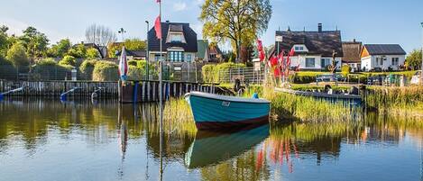 A calm lake with a docked boat, a pier, and houses in the background.