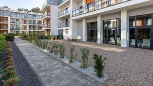 A modern multi-story residential building with balconies, a paved walkway, and a landscaped garden area. - Comfortable Apartment, Pool, Close to the Beach (Rewal)