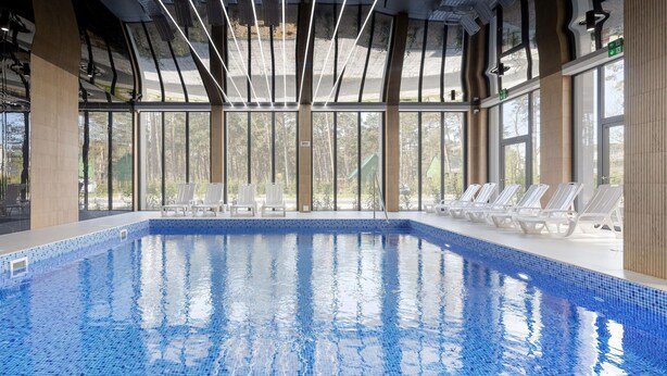 An indoor swimming pool with clear blue water, surrounded by large windows and white lounge chairs. - Comfortable Apartment, Pool, Close to the Beach (Rewal)