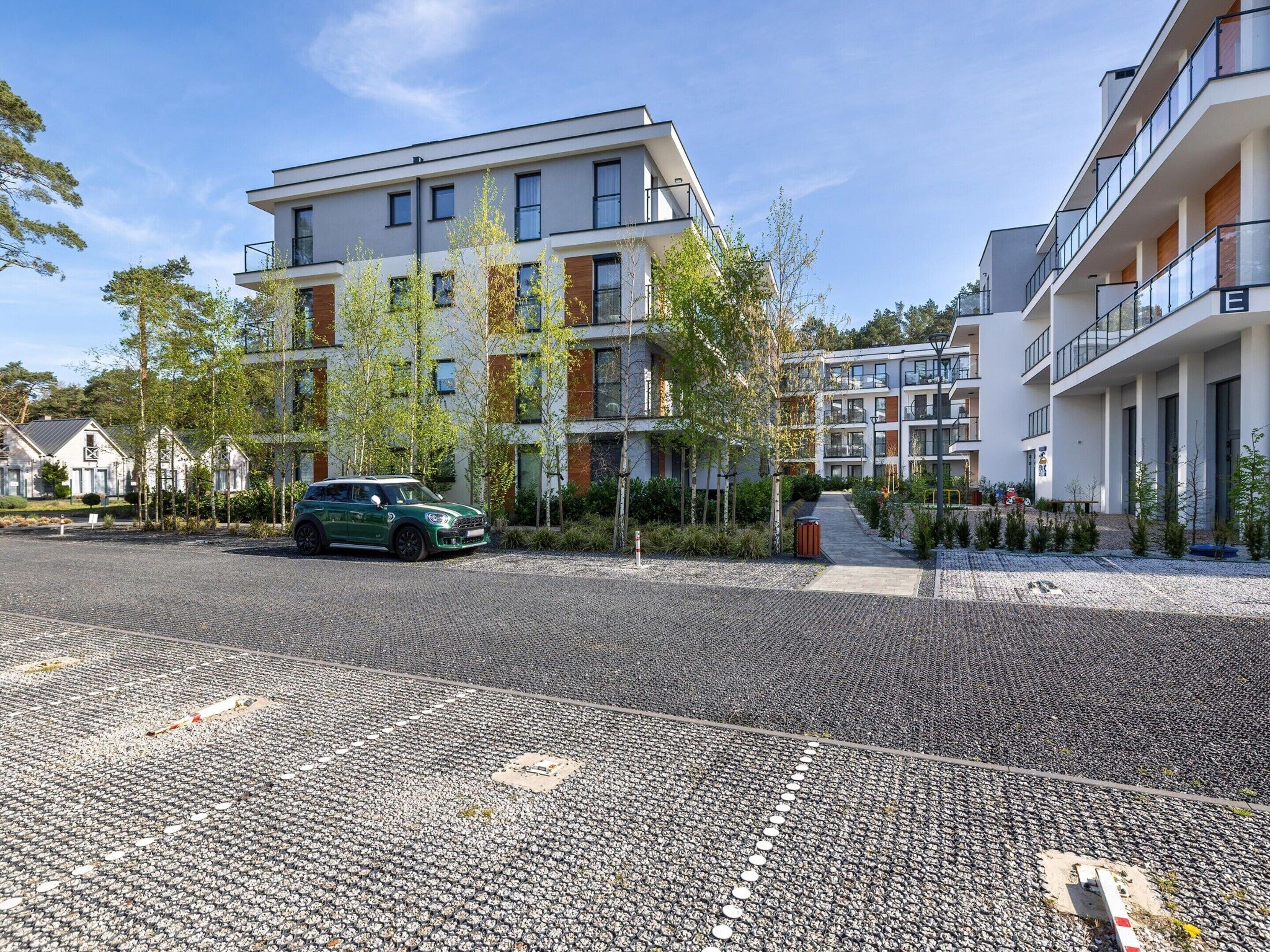 Ein modernes Apartmenthaus mit einer Schotterauffahrt und einem grünen Auto davor.
