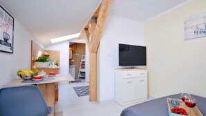 Ein modernes, kompaktes Zimmer mit einem Bett, einem Fernseher, einem Schreibtisch mit Stuhl und einer Essecke.