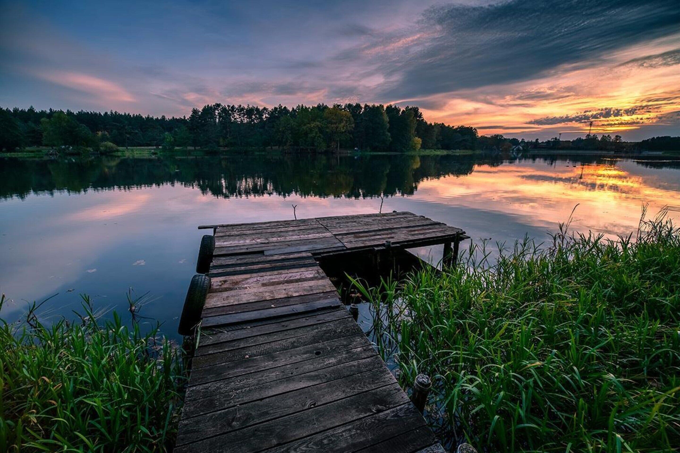 A wooden dock extending into calm water with a forested shoreline in the background.