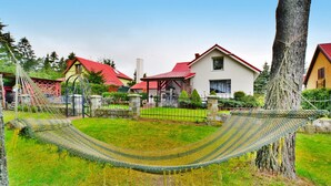 A hammock between trees in a grassy area with houses in the background. - Spacious Cottage, Idyllic Right on the Lake, Spore (Szczecinek)