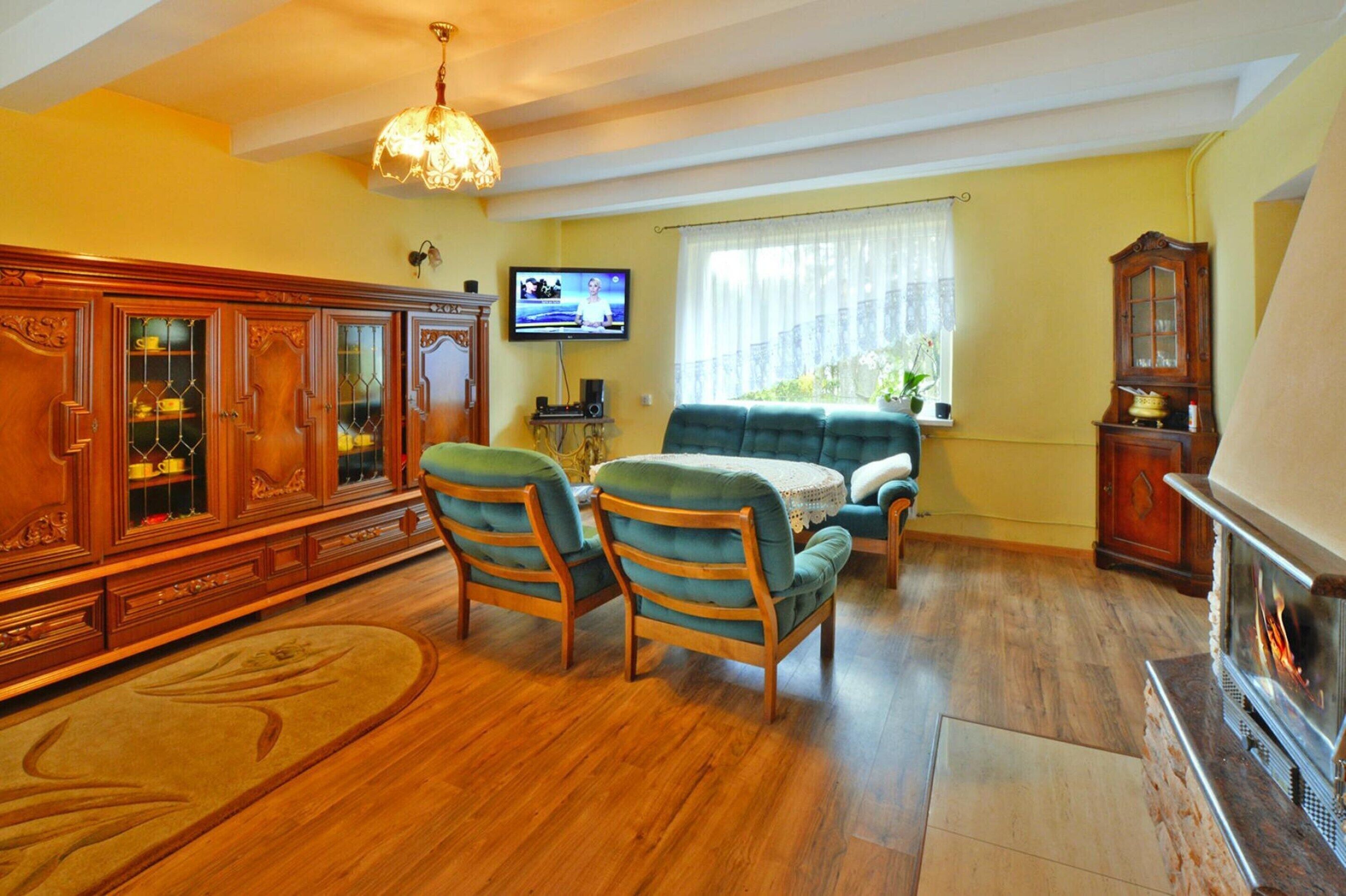 A living room with wooden flooring, a green sofa, two chairs, a television, a fireplace, and a large wooden cabinet.