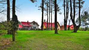 A grassy area with trees and houses with red roofs. - Spacious Cottage, Idyllic Right on the Lake, Spore (Szczecinek)
