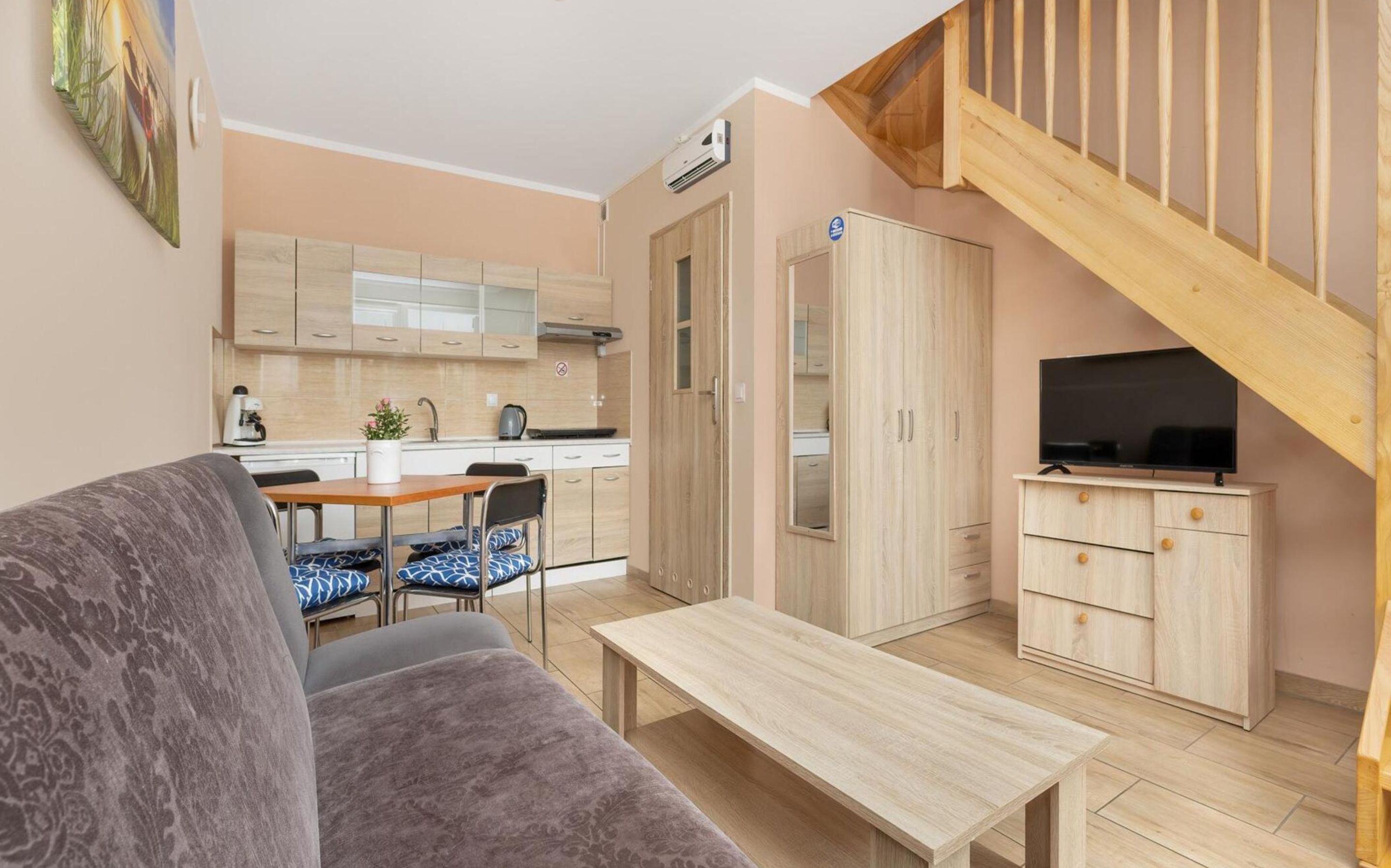 Ein kompakter Wohnbereich mit Küchenzeile, Essbereich, Sofa, Fernseher und einer Treppe.