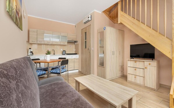 A compact living space with a kitchenette, a dining area, a sofa, a TV, and a staircase. - Apartment in Niechorze Near Baltic Beach (Rewal)