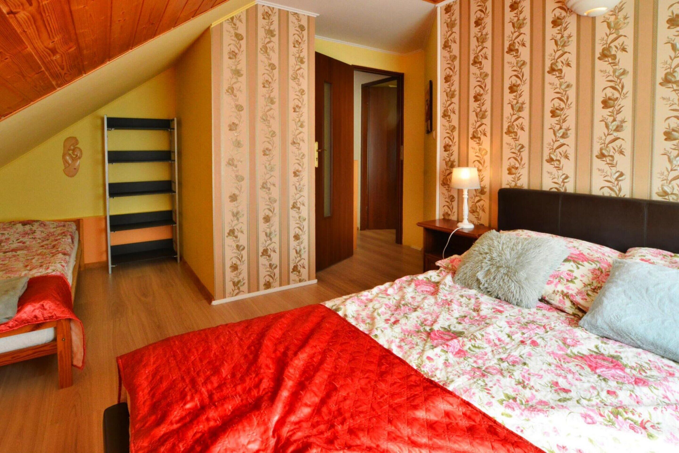 A bedroom with a wooden ceiling, a bed with floral bedding, a red throw blanket, and a nightstand with a lamp.