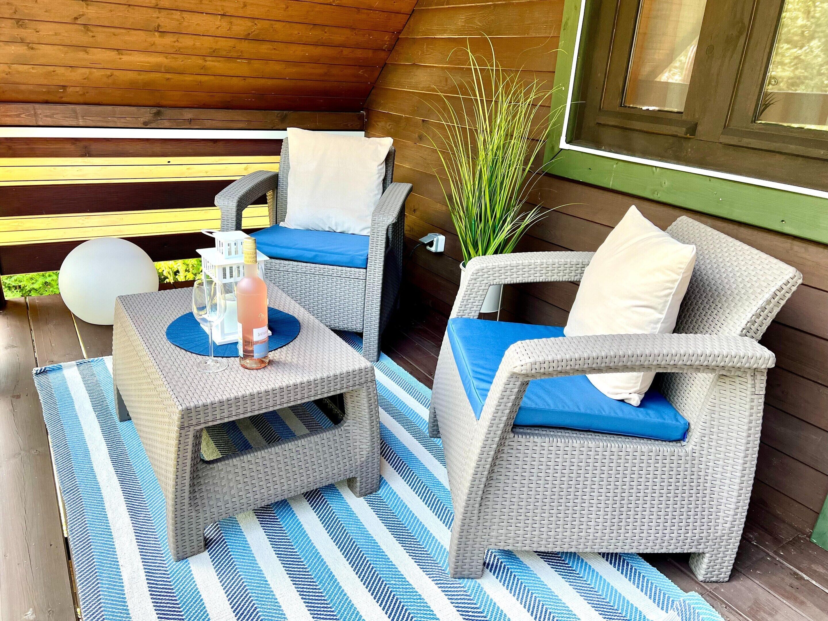A covered outdoor seating area with wicker furniture, blue cushions, and a striped rug.