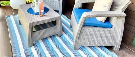 A covered outdoor seating area with wicker furniture, blue cushions, and a striped rug.