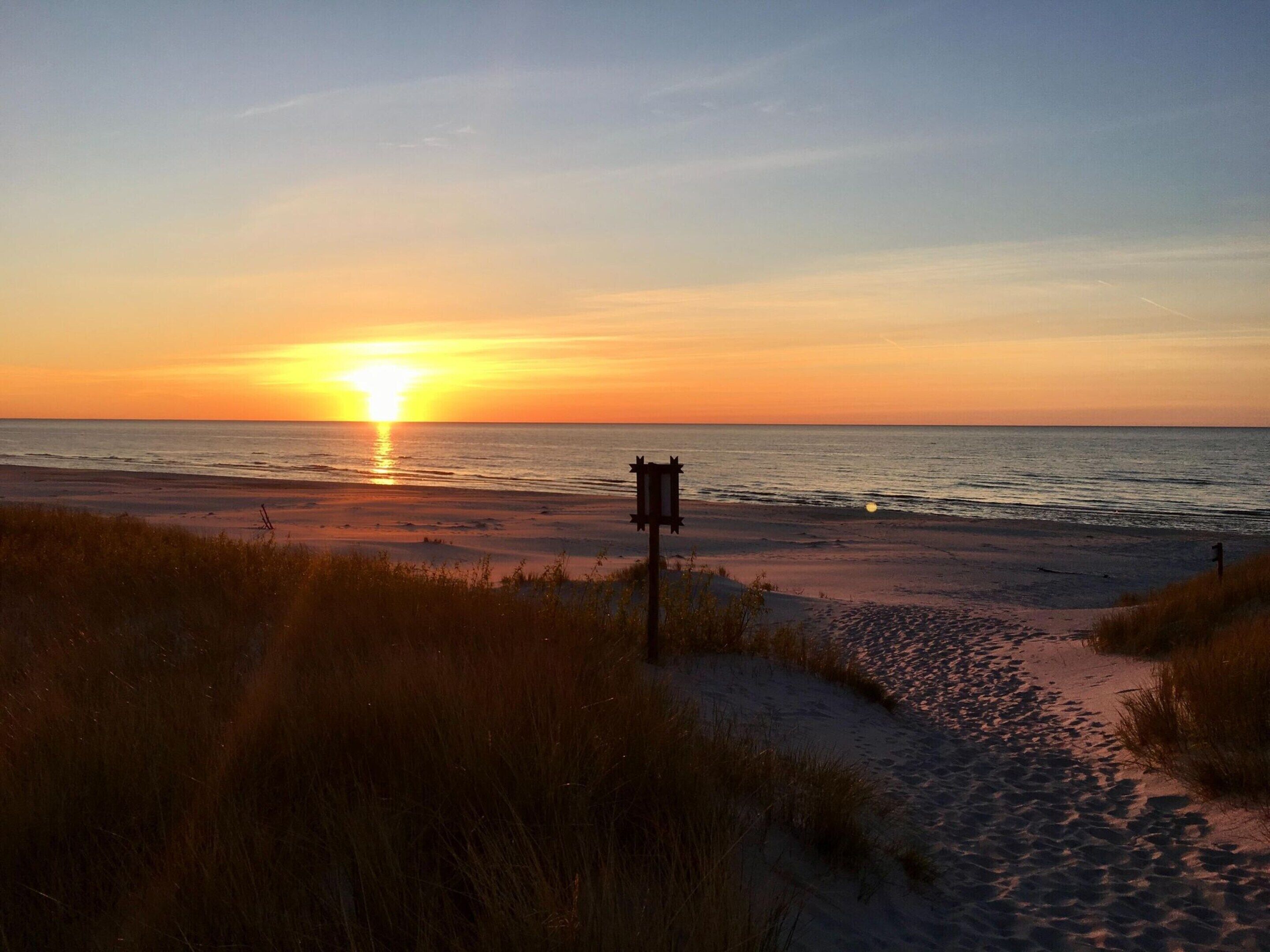 Una playa al atardecer con un letrero de madera en primer plano.
