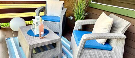 A patio with wicker furniture, a striped rug, and a bottle of wine.