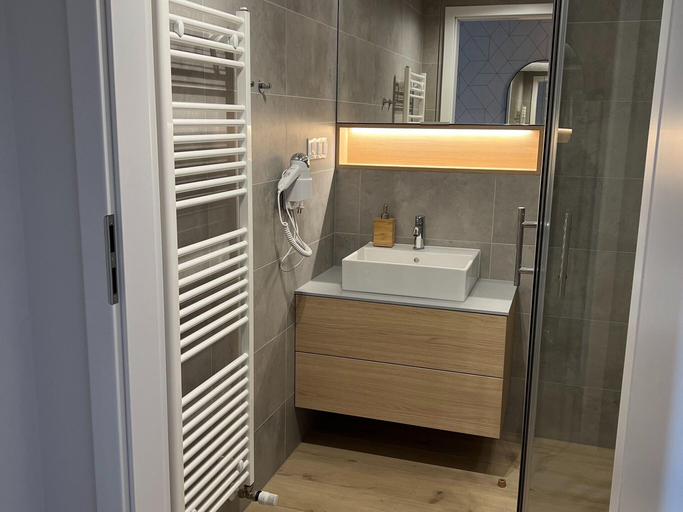 Un baño moderno con calefacción integrada, un lavamanos con gabinete de madera y un espejo sobre el lavamanos.