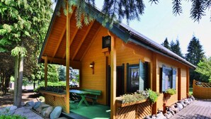 A wooden cabin with a covered porch, a picnic table, and a window with shutters.