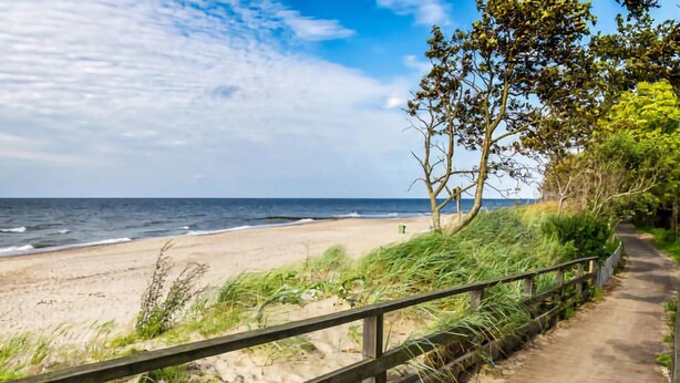 A wooden boardwalk along a beach with a sandy shore and ocean in the background.