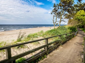 A wooden boardwalk along a beach with a sandy shore and ocean in the background.