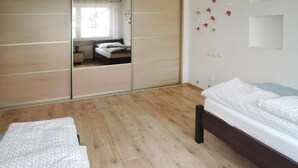 A bedroom with a wooden floor, a bed with patterned bedding, a wardrobe with a mirror, and a small window with curtains. - Holiday Appartment in Stepnica for 4 Persons (Stepnica)