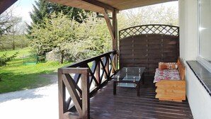 A wooden deck with a glass table and chairs, a cushioned bench, and a view of a garden and trees. - Holiday Appartment in Stepnica for 4 Persons (Stepnica)
