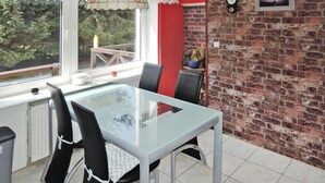 A dining area with a glass table and chairs, a view of greenery outside, a brick wall, and a clock on the wall. - Holiday Appartment in Stepnica for 4 Persons (Stepnica)
