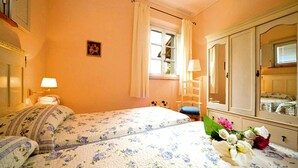 A hotel room with a bed, a dresser, a mirror, a window with curtains, and a small table with a lamp. - Apartment in Tuscany With Golf & Pools (Gambassi Terme)