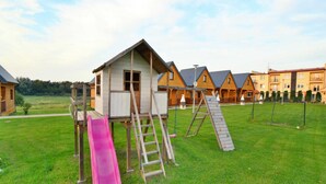 A playground with a slide, climbing net, and a small wooden house. - Holiday Home Ustronie Morskie Near Beach (Ustronie Morskie)