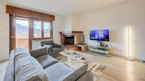 Ein modernes Wohnzimmer mit Sofa, Couchtisch, Kamin, Fernseher und Blick durch große Fenster.