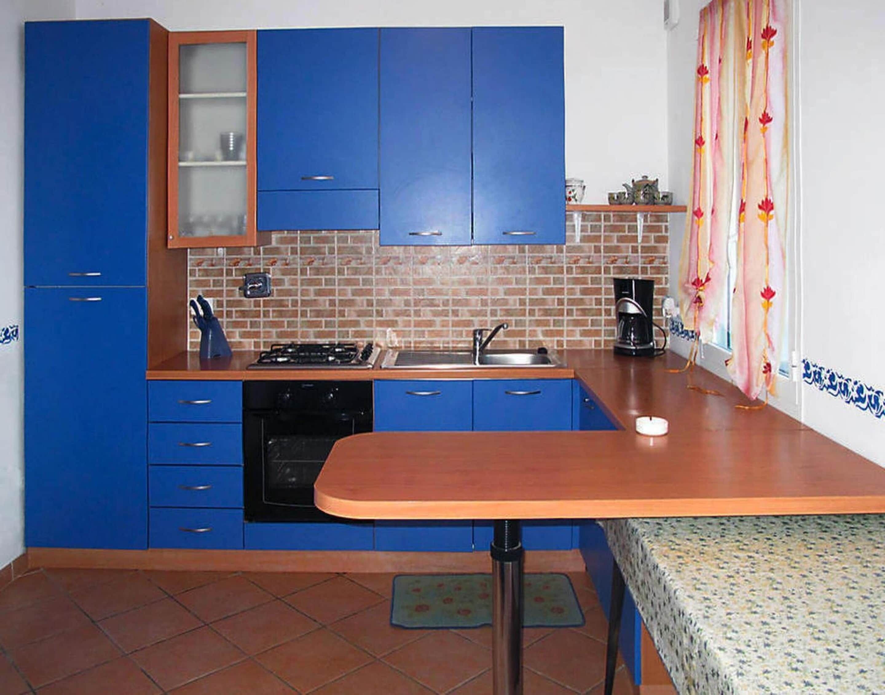 Une cuisine de taille réduite avec des meubles bleus, une cuisinière à gaz, un évier et une machine à café.