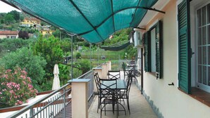 A balcony with a table and chairs, a green awning, and a view of greenery and buildings. - Apartment in Imperia With Communal Pool (Imperia)