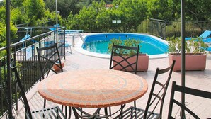 A covered outdoor area with a pool, seating, and a view of the surrounding greenery and buildings. - Apartment in Imperia With Communal Pool (Imperia)