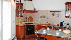 A kitchen with wooden cabinets, a stove, a sink, and a dining area with bar stools. - Apartment in Imperia With Communal Pool (Imperia)