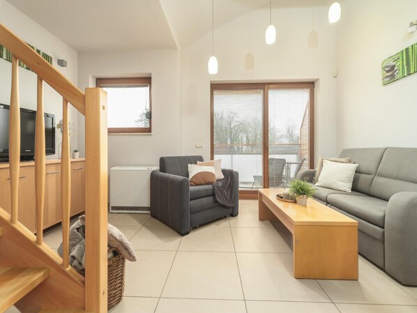 A modern living room with a grey sofa, a wooden coffee table, a grey armchair, and a TV on a wooden cabinet. - Apartment in Rewal by Baltic Sea Beach (Rewal)