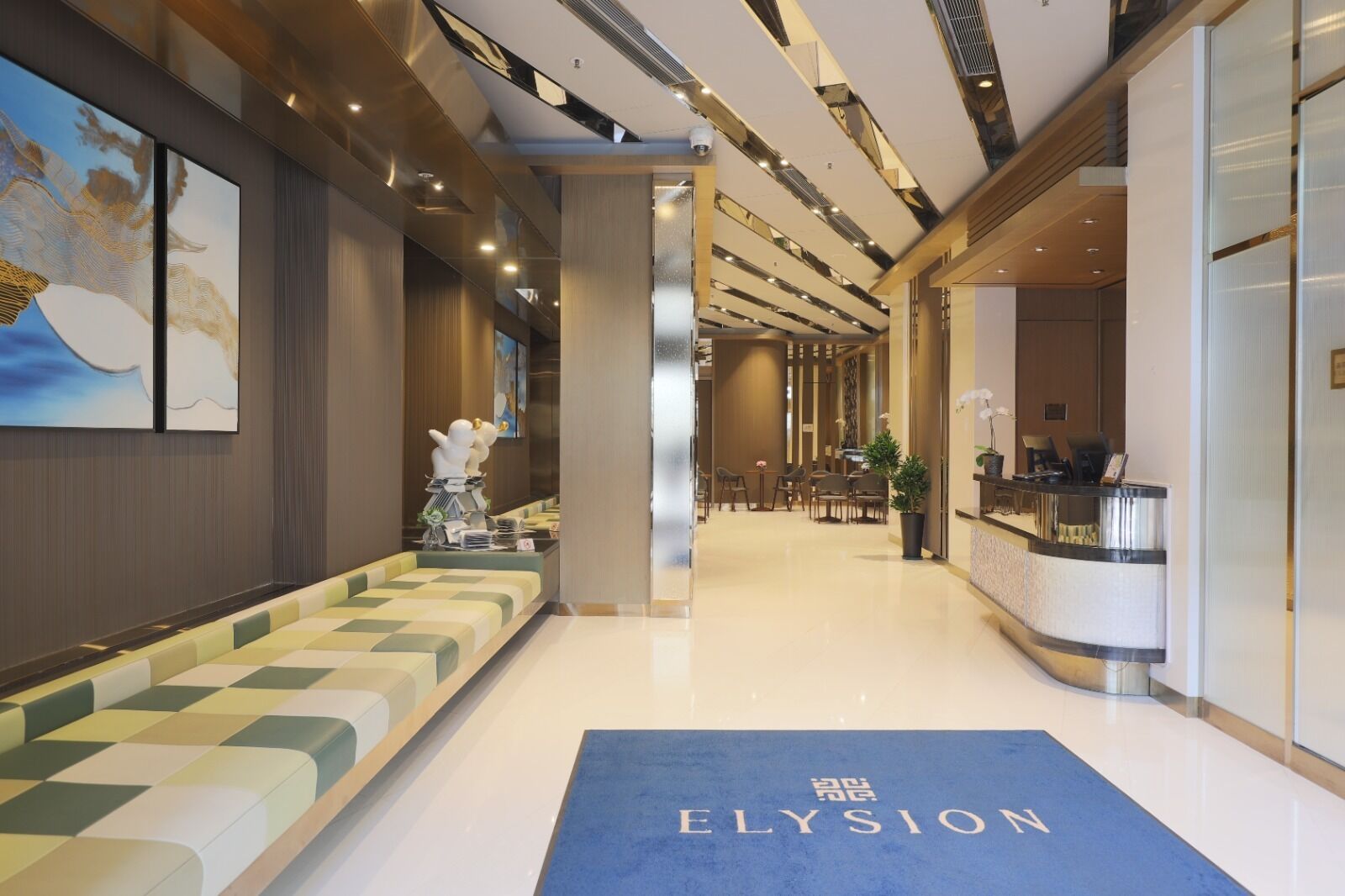 En moderne hotellobby med reception, siddeområde og et blåt tæppe med teksten "ELYSION".