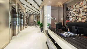 Een moderne hotellobby met een receptiebalie, zithoek en decoratieve wand.