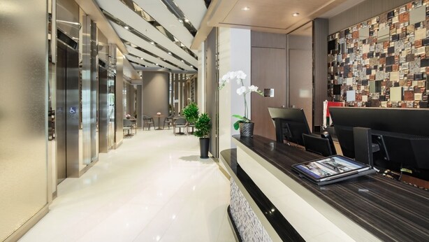 Een moderne hotellobby met een receptiebalie, zithoek en decoratieve wand.
