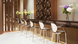 Een bar met een lange toonbank, diverse barkrukken en decoratieve vazen met bloemen.