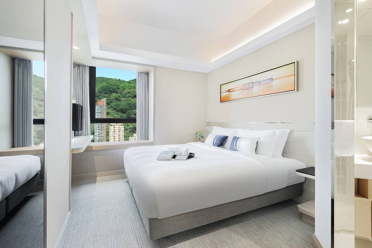 Une chambre d’hôtel moderne avec un grand lit, une vue sur la verdure et un tableau au mur.