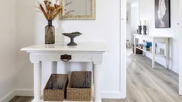 A white console table with a mirror, a vase with dried flowers, and two wicker baskets.