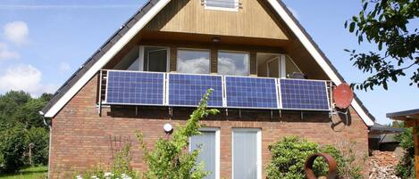 Ein zweistöckiges Haus mit geneigtem Dach, Solaranlagen im zweiten Stock, einem kleinen Fenster und einer Tür.