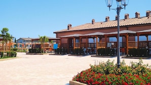 A spacious outdoor area with a building featuring a tiled roof and wooden latticework. - Apartment in Vada With Garden Furniture (Rosignano Marittimo)