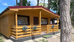 A wooden cabin with a porch, windows, and a small outdoor area with steps. - New Houses Available Near the sea in Dziwnowek (Dziwnów)