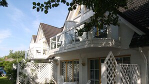 Ein zweistöckiges Haus mit Balkon, einer Terrasse und Gartenmöbeln sowie einem weißen Zaun.