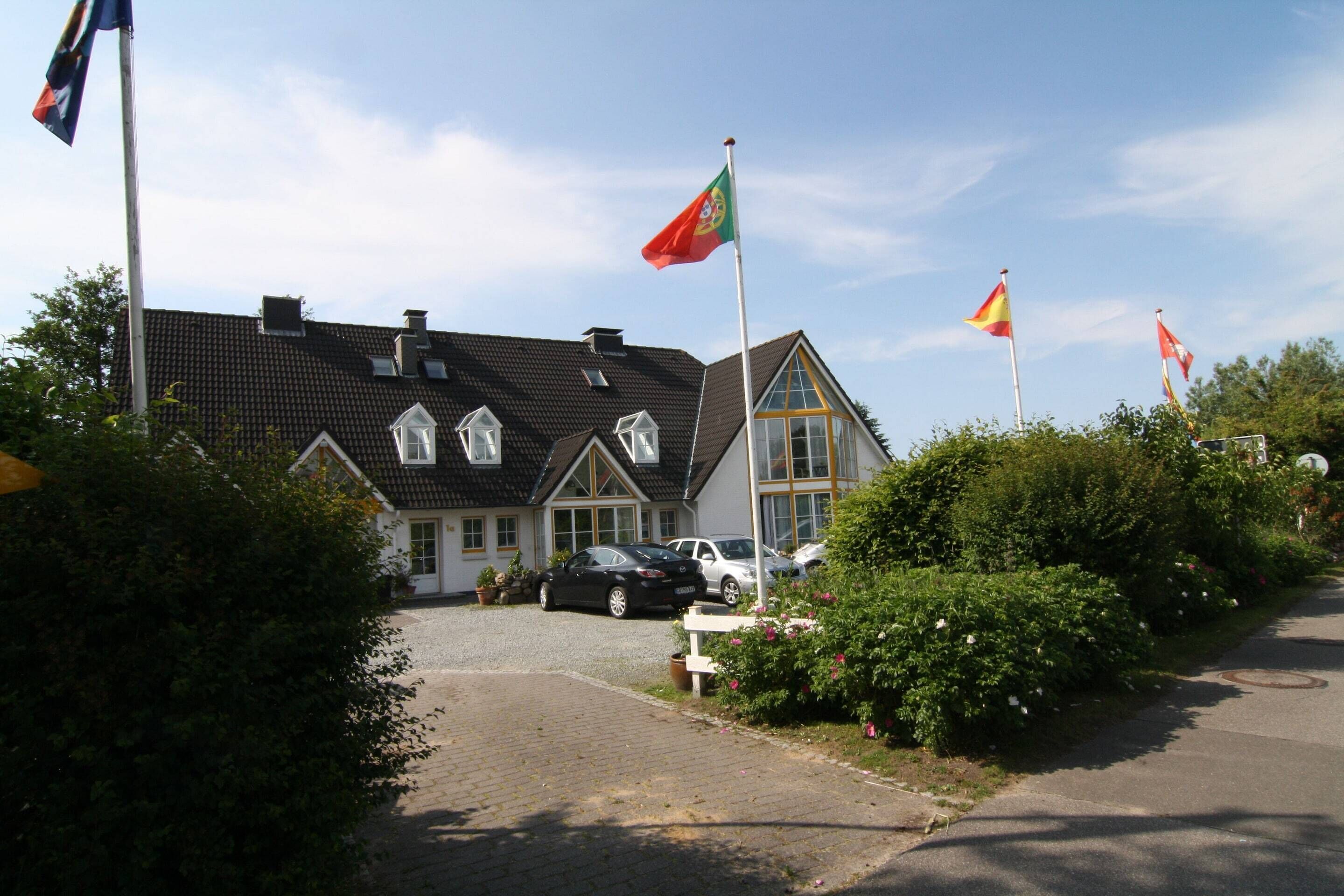 A house with a paved driveway, a car parked in front, and multiple flags on flagpoles.