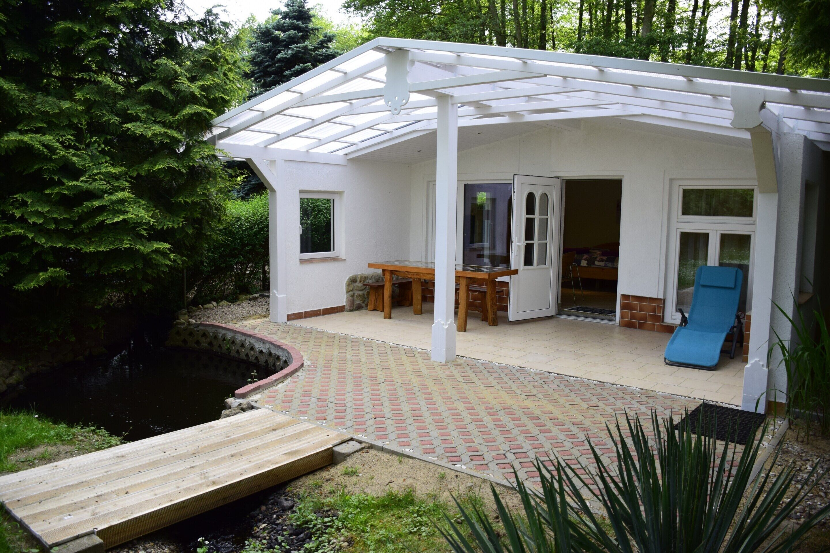 A covered patio area with a wooden deck, a table and chairs, a blue mat, and a small pond.