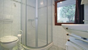 Un baño con inodoro, ducha con mampara de vidrio y lavabo con ventana.